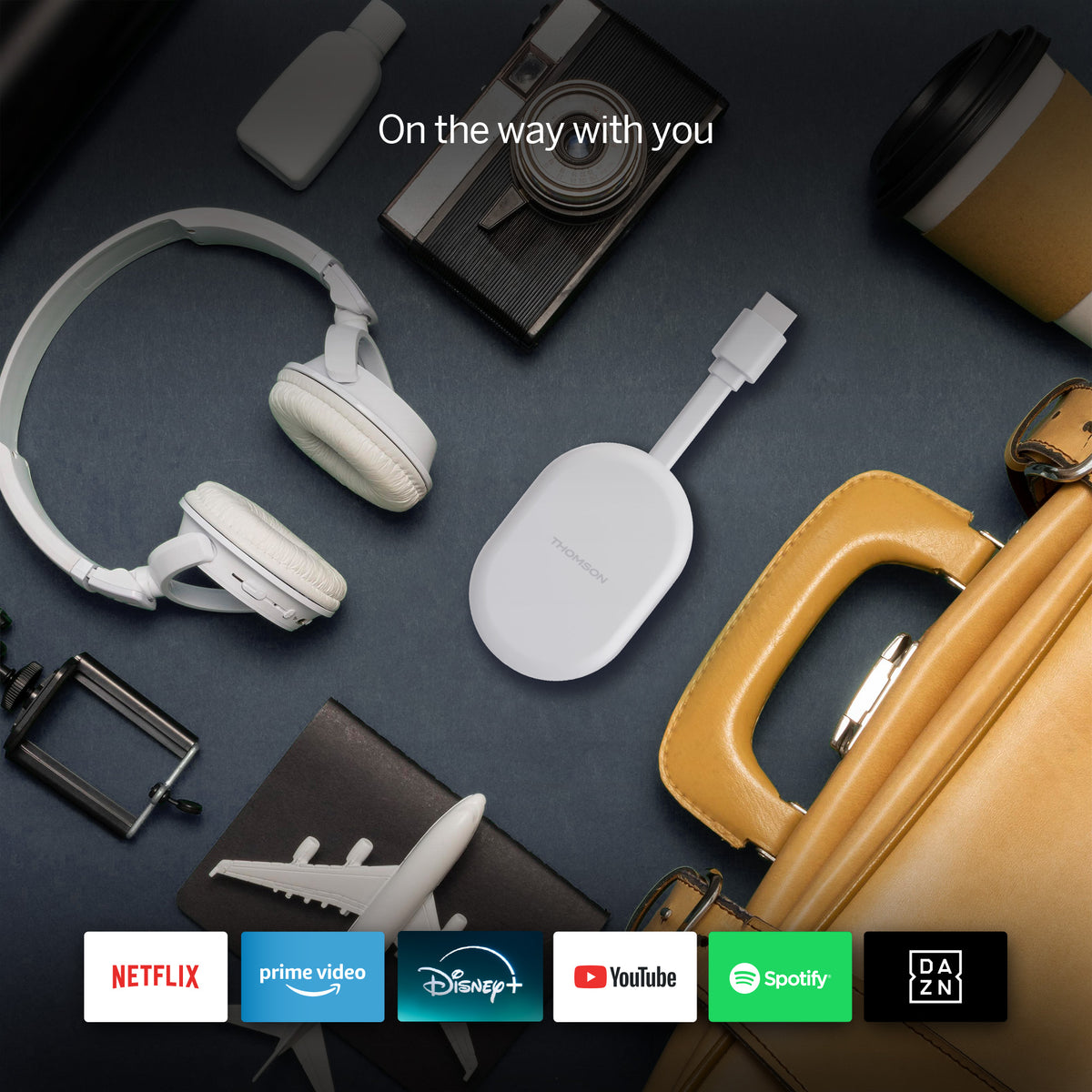 Collection of electronic devices, streaming dongle and a handbag on a dark surface with streaming service logos at the bottom.