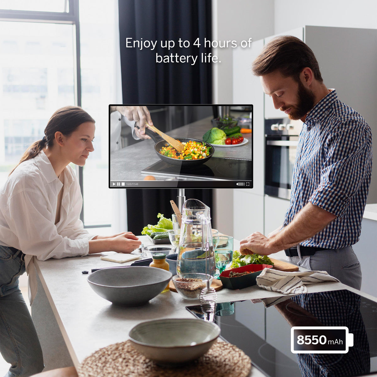 Man and woman preparing food in a kitchen with a screen displaying cooking instructions.